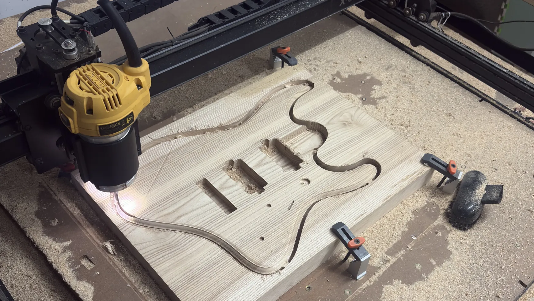 A CNC router cutting the Solic Arc body outline and pickup cavities from an ash blank, with sawdust around it.