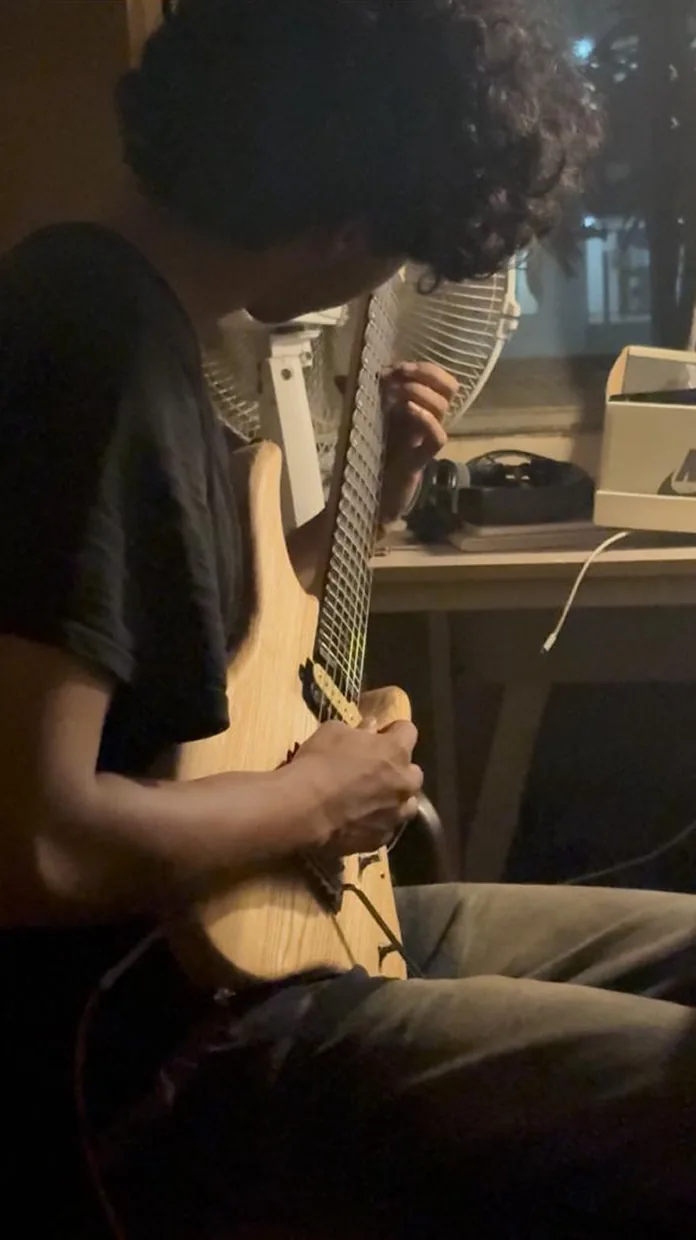 A player looks down at the fretboard while playing seated.