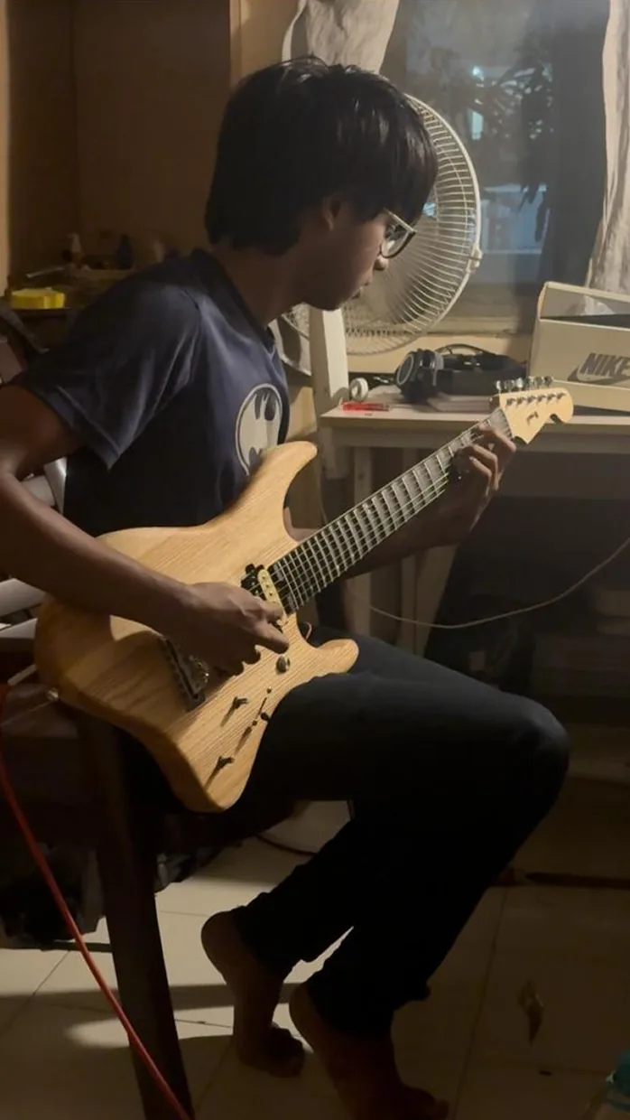 A player seated on a chair, guitar across his leg.