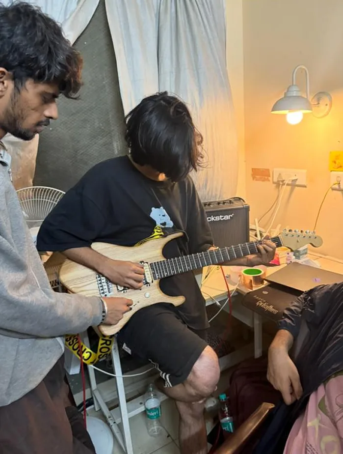 A player seated with the guitar while a friend watches.