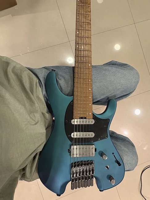 Top-down view of a headless guitar resting on a seated player's thigh.