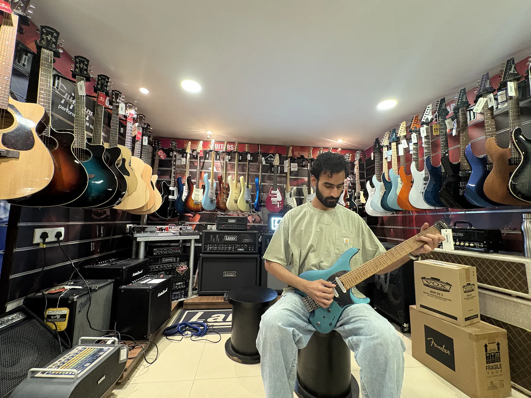 Anshul seated in a music store, holding a teal headless guitar, surrounded by guitars on the walls.