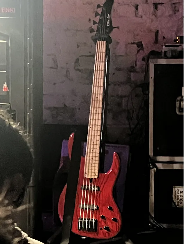A red five-string bass on a stand on stage.